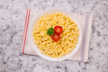 Macaroni and cheese on a white plate with parsley and cherry tomatoes on a gray background
