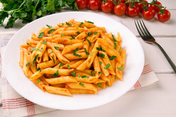 Penne pasta in tomato sauce, decorated with parsley on a white wooden table