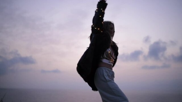 Slow Motion Shot Of Carefree Woman Dancing In Illuminated Clothing By Sea Over Grass During Sunset - Negev, Israel