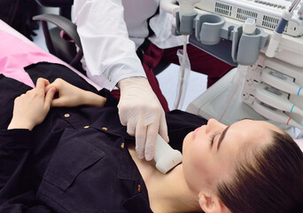 the doctor performs an ultrasound examination of the thyroid gland of a young, pretty woman in a...