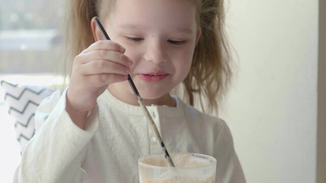 A little girl plays with a milkshake. The baby blows into the milkshake, and bubbles come out of it. Concept, child's play