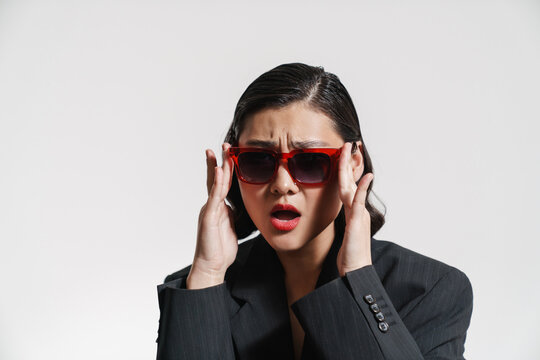 Brunette asian woman wearing jacket and sunglasses frowning at camera