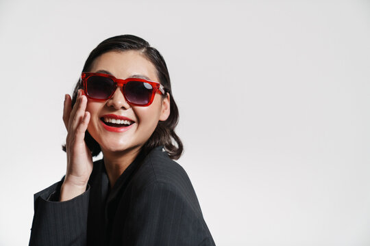 Brunette asian woman wearing jacket and sunglasses smiling at camera