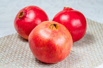 Three red pomegranates on a beige wicker rug