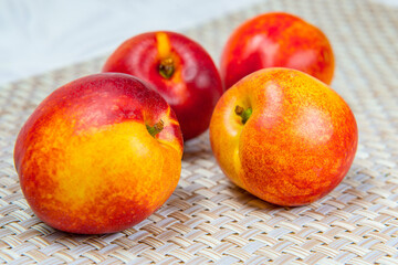 Four ripe nectarines on a beige wicker rug