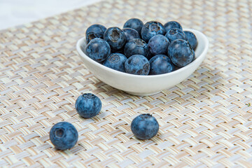 A small white uneven plate of fresh blueberries on a beige wicker mat