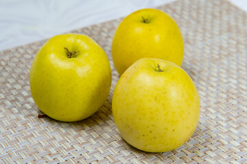 Three golden delicious apples on a beige wicker mat