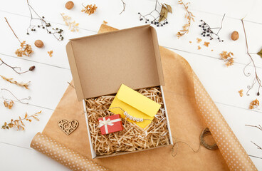 Eco friendly packaging of a gift box in a paper wrap. Top view on white wooden background Decorated by Autumn leaves. Donation. Zero waste. Autumn present. Craft present box. Fall party celebration. 