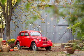 Autumn decorations with red retro car and lamp garland on background. Outdoor. Harvest celebrating. Pumpkin and lantern on the grass. Halloween celebration