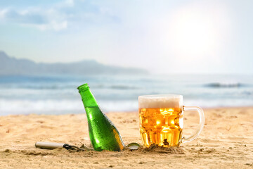 Bottle and mug of fresh beer on sand at beach