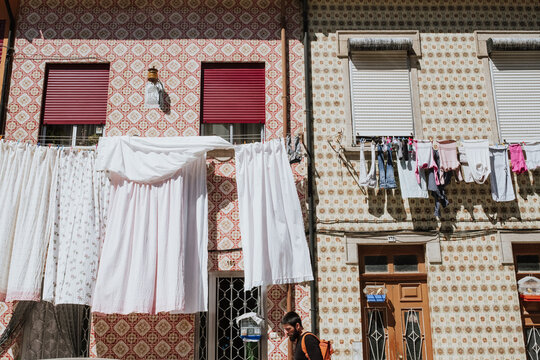 A young traveler walking on a traditional street with 
clothes hanging and old tiled walls in Afurada, Porto