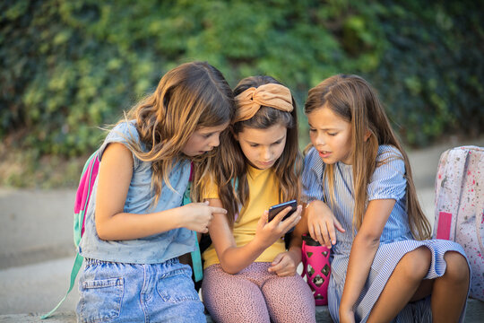 Three school  little girls using smart phone together.
