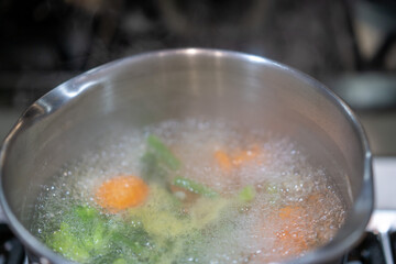 cooking pot with vegetables, vegetables cooking in water in pot on stove top
