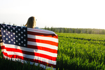 4th of July. Independence Day. Beautiful young woman with  American flag in a wheat field. 