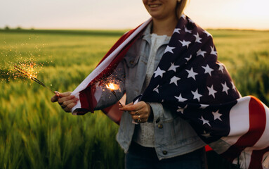 Young girl holding bengal fire with American flag at sunset. America celebrate 4th of July....