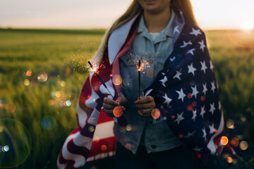 Young girl holding bengal fire with American flag at sunset. America celebrate 4th of July....