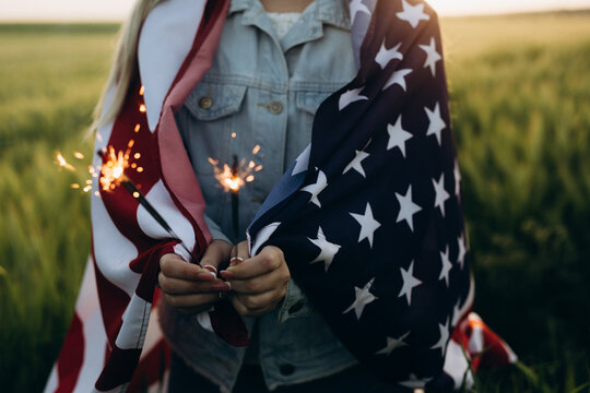Young girl holding bengal fire with American flag at sunset. America celebrate 4th of July. Independence Day.