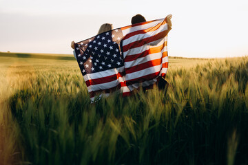 Patriotic holiday. Young couple with the American flag in a wheat field at sunset. Independence Day, 4th of July.
