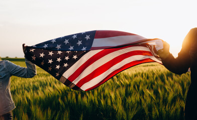 Patriotic holiday. Young patriotic couple with the American flag in a wheat field at sunset....