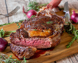 Grilled rib eye or tomahawk steak on wooden cutting board with herbs