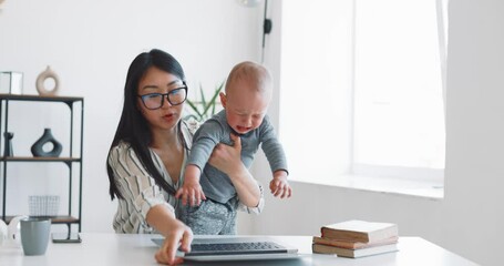 Young mother freelancer with her child working at home office using laptop - Powered by Adobe