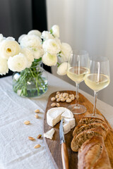Two glasses of white wine and a wooden board with appetizers on the table.