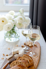 Two glasses of white wine and a wooden board with appetizers on the table.