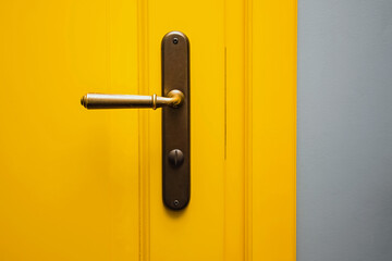 Yellow door with a bronze door handle close-up.