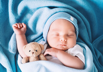 Newborn sleep at first days of life. Portrait of new born baby one week old with cute soft toy in crib in cloth background. - obrazy, fototapety, plakaty