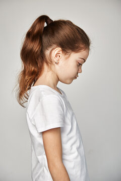 A cute 10-year-old model with an oriental appearance expresses sadness, dressed in a white T-shirt. Portrait of a studio shot on a white copy space. Expression of emotions