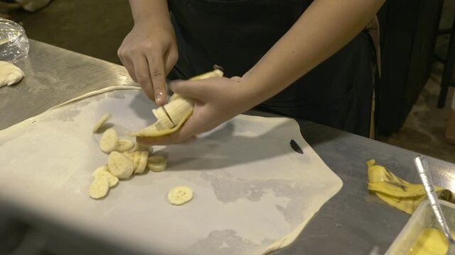 Unrecognizable local street food vendor preparing roti, cutting, adding banana to stretched thin layer dought on counter top, flip and fold the roti by using barehand. Asian night flea market concept.