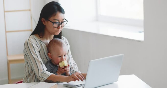 Young mother freelancer with her child working at home office using laptop