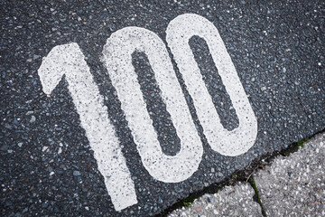 number 100 white painted on the grey road , sign on the asphalt