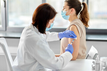 health, medicine and pandemic concept - female doctor or nurse wearing protective medical mask and gloves with syringe vaccinating patient at hospital