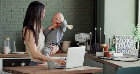 Freelance woman with a small child tries to work on a laptop in the kitchen. Home business concept.