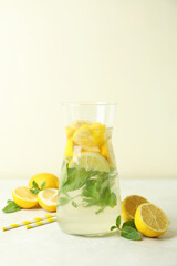 Jug of lemonade, lemons and straws on white textured table