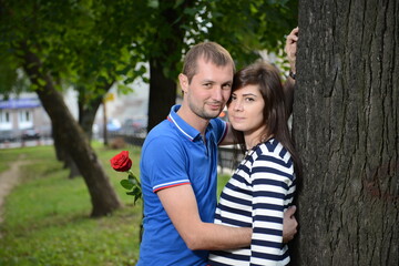 A guy and a girl with a rose are pressed against a tree. - 435790519