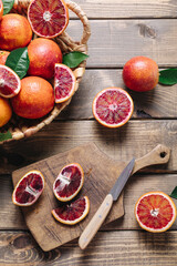 Whole and sliced blood oranges with knife and chopping board over wooden table background. Summer cocktails and fresh orange juice cooking concept. Flat lay, top view.