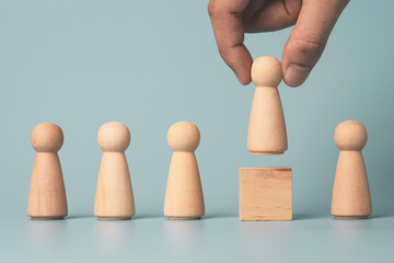 Hand putting wooden figure on wooden cube block on blue background , promotion to leadership and management growth concept.