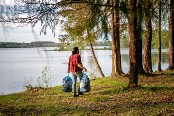 Naklejka na ściany i meble Young man with bags of trash cleaning the green forest from household rubbish, environmental problems and recycling of plastic.