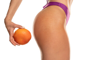 female hip with stretch marks and cellulite and orange in hand