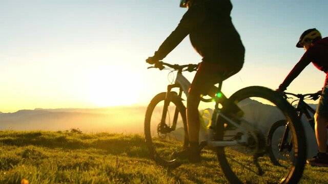 Happy mother and daughter riding mountain bikes, across the meadow, stopping at the top of the hill, giving high five and enjoying an amazing view
