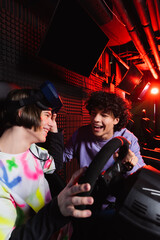 cheerful teenage guys talking near car racing simulator in vr game room