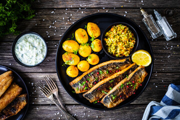 Fried herring fillets with potatoes and vegetable salad  on wooden table
