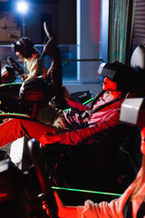 Obraz na płótnie Canvas amazed gamer racing on car simulator near blurred friends