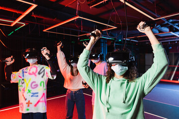 interracial gamers in medical masks and vr headsets showing win gesture