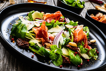 Tasty salad - ham, parmesan and fresh vegetables on wooden background
