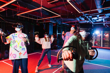 multiethnic friends in medical masks and vr headsets having fun in play room
