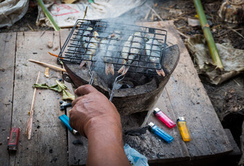 Hand to grate the grill to grill the fish, Grilled fish in a grill on the stove, local way of life, local food.