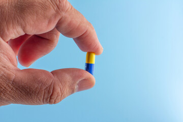 Fototapeta premium Hand is holding an antibiotic capsule (blue-yellow) isolated on a blue background.